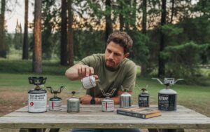 Camper comparing portable camp stoves and fuel options at a campsite to decide which stove to use